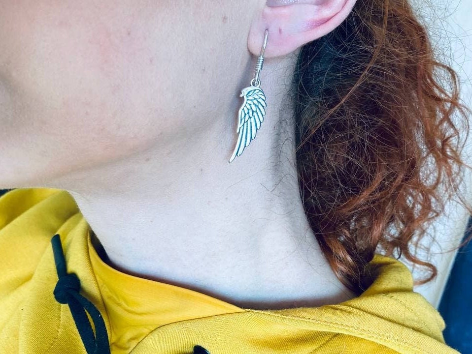 Woman wearing a silver angel wing drop earring, side view