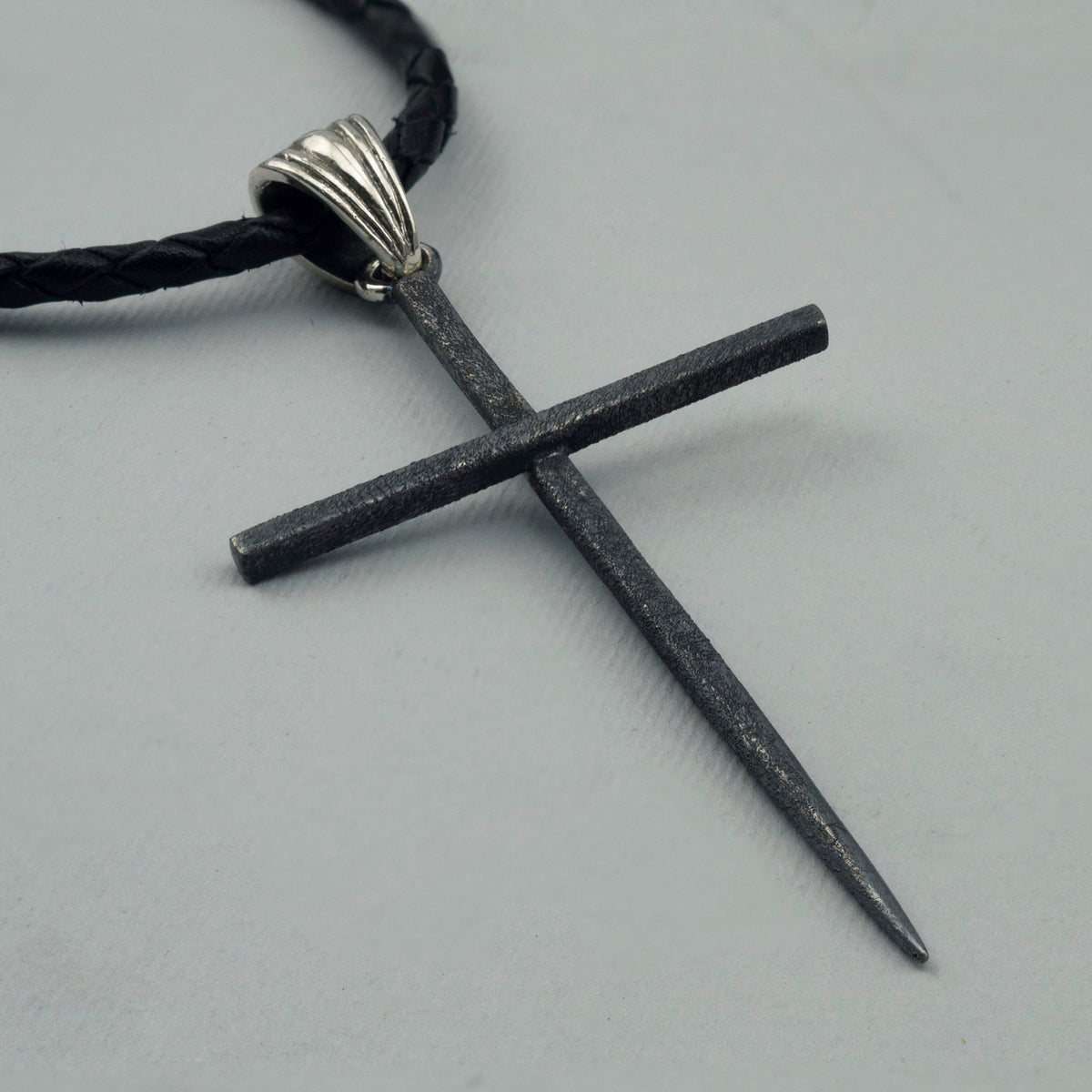 Close-up of the matte black spike cross pendant and polished ribbed bail on leather cord