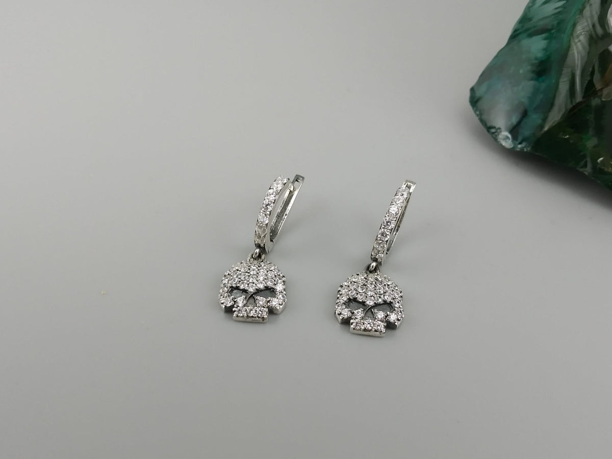Crystal Skull drop earrings lying on gray, wide view