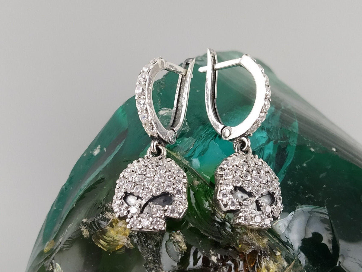 Crystal Skull CZ drop earrings hanging over a green glass stone