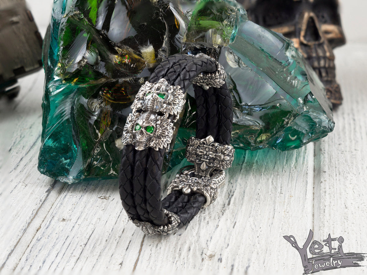 Garry braided black leather bracelet with silver feathered skulls and green eyes