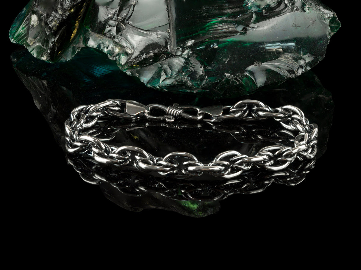 Graf silver bracelet resting on a dark rock, angled view