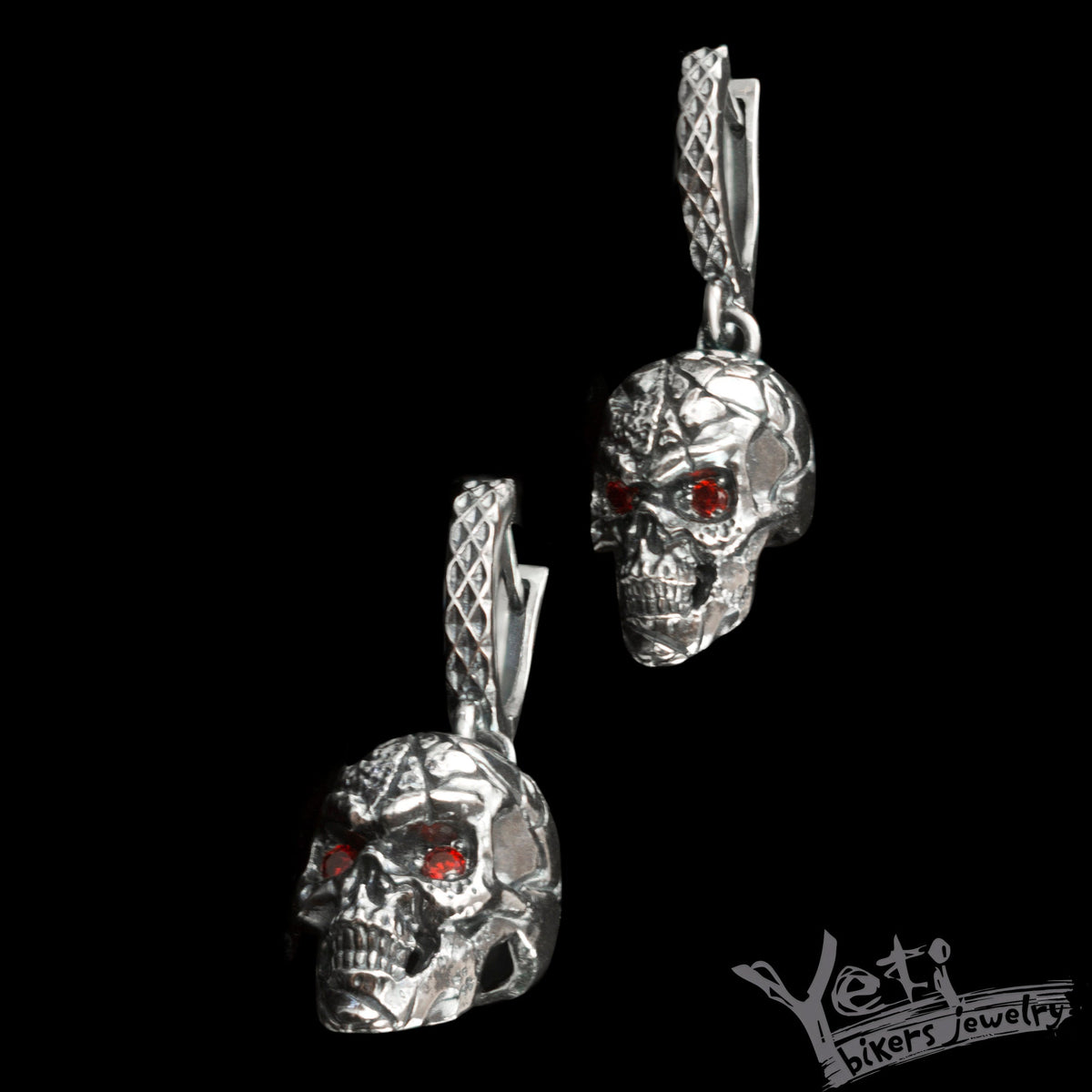 Silver skull dangle earrings with red eyes, angled hanging view
