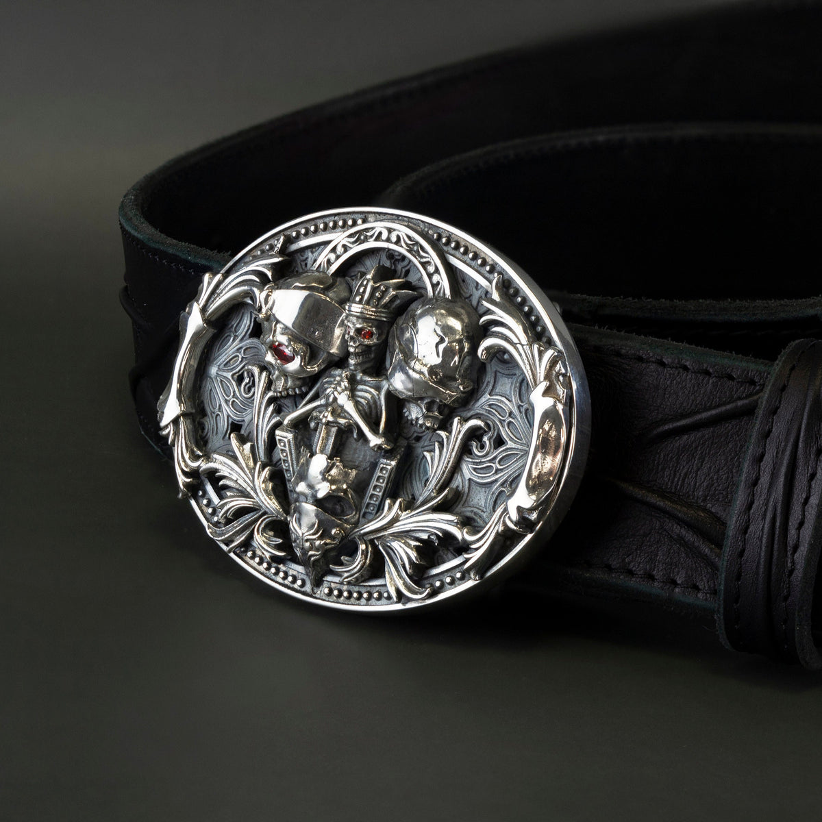 Sterling silver skull belt buckle on a black leather belt, angled view