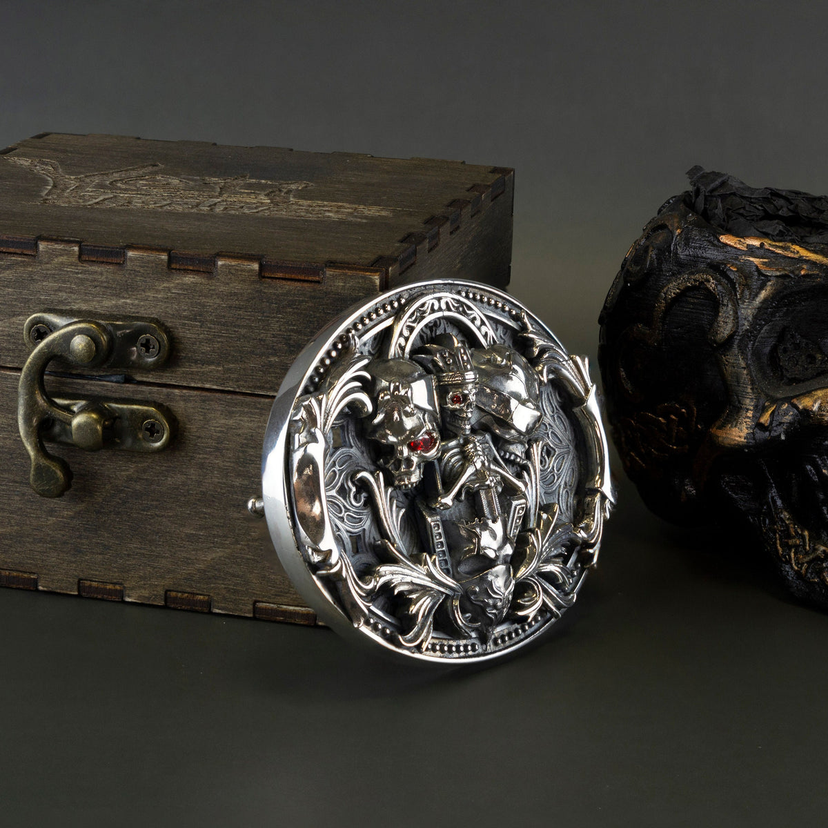 Heavy silver skull buckle standing next to a wooden box, side angle