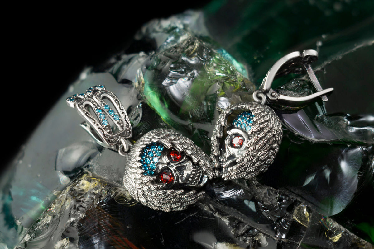 Annabelle sterling silver skull earrings with textured skull designs, red and blue cubic zirconia stones, and decorative silver ear fittings.