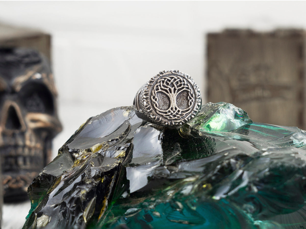 Yggdrasil Tree of Life ring in 925 sterling silver with intricate circular knotwork and oxidized detailing, photographed on a textured mineral background.