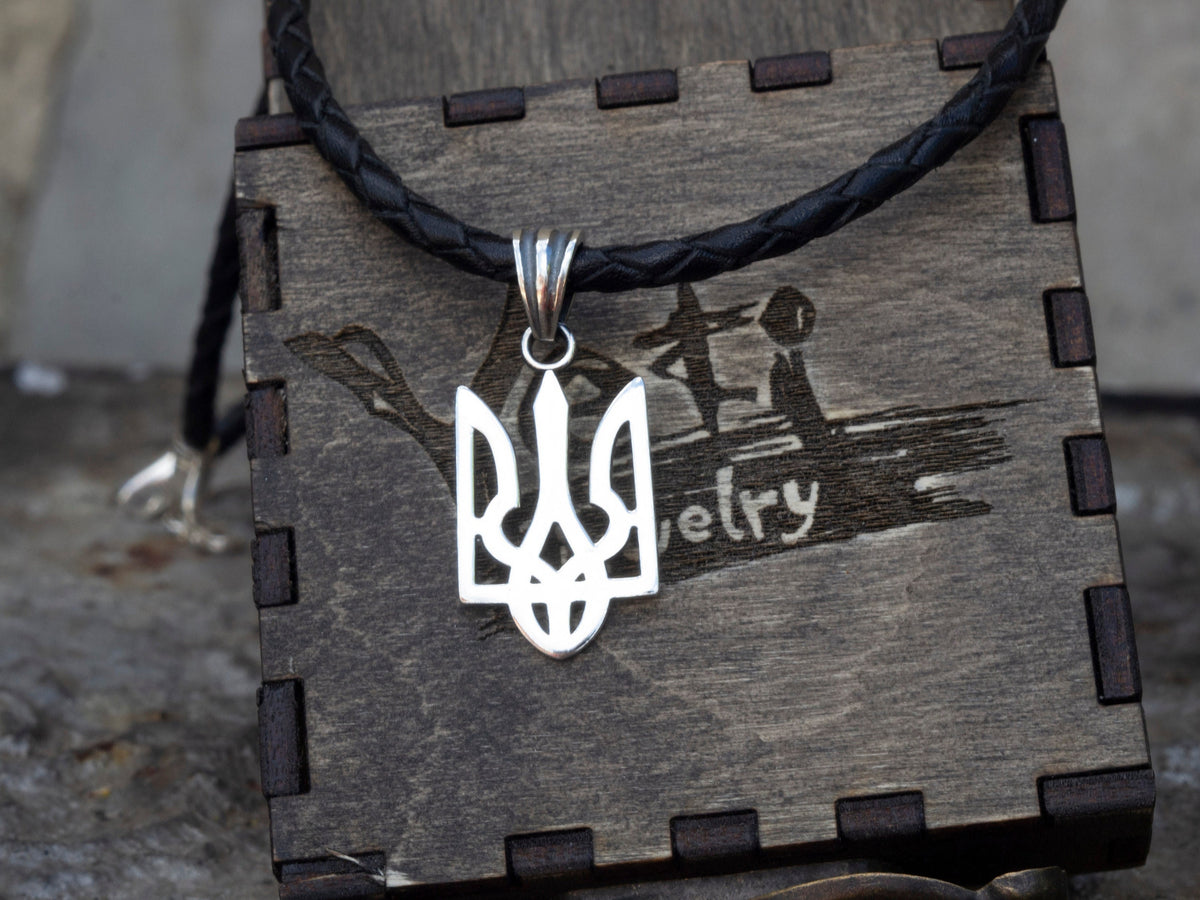 Ukrainian Tryzub pendant in polished 925 sterling silver displayed on a black braided leather cord against a branded wooden jewelry box.