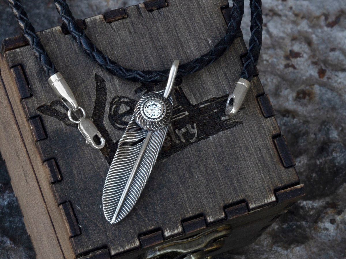 Textured Feather pendant in 925 sterling silver with a round cubic zirconia setting, shown with a black braided leather cord on a wooden Yeti Jewelry box.