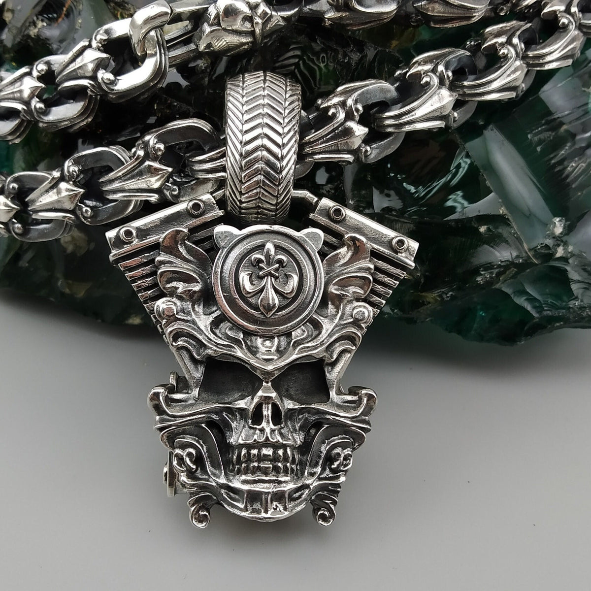 Vigor V-Twin skull pendant in 925 sterling silver with an ornamental fleur-de-lis-inspired emblem and sculpted mechanical details, photographed with a silver biker chain.