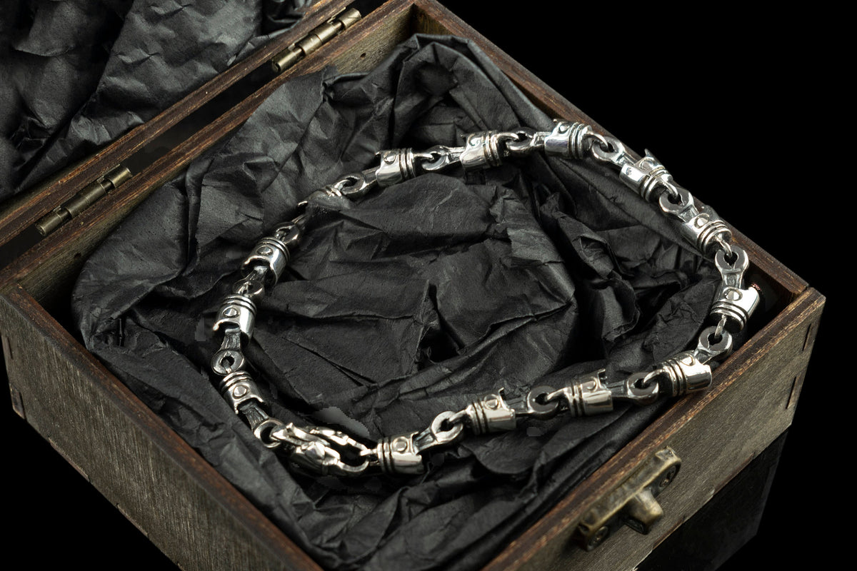 Piston and rod biker bracelet resting inside an open box on black paper