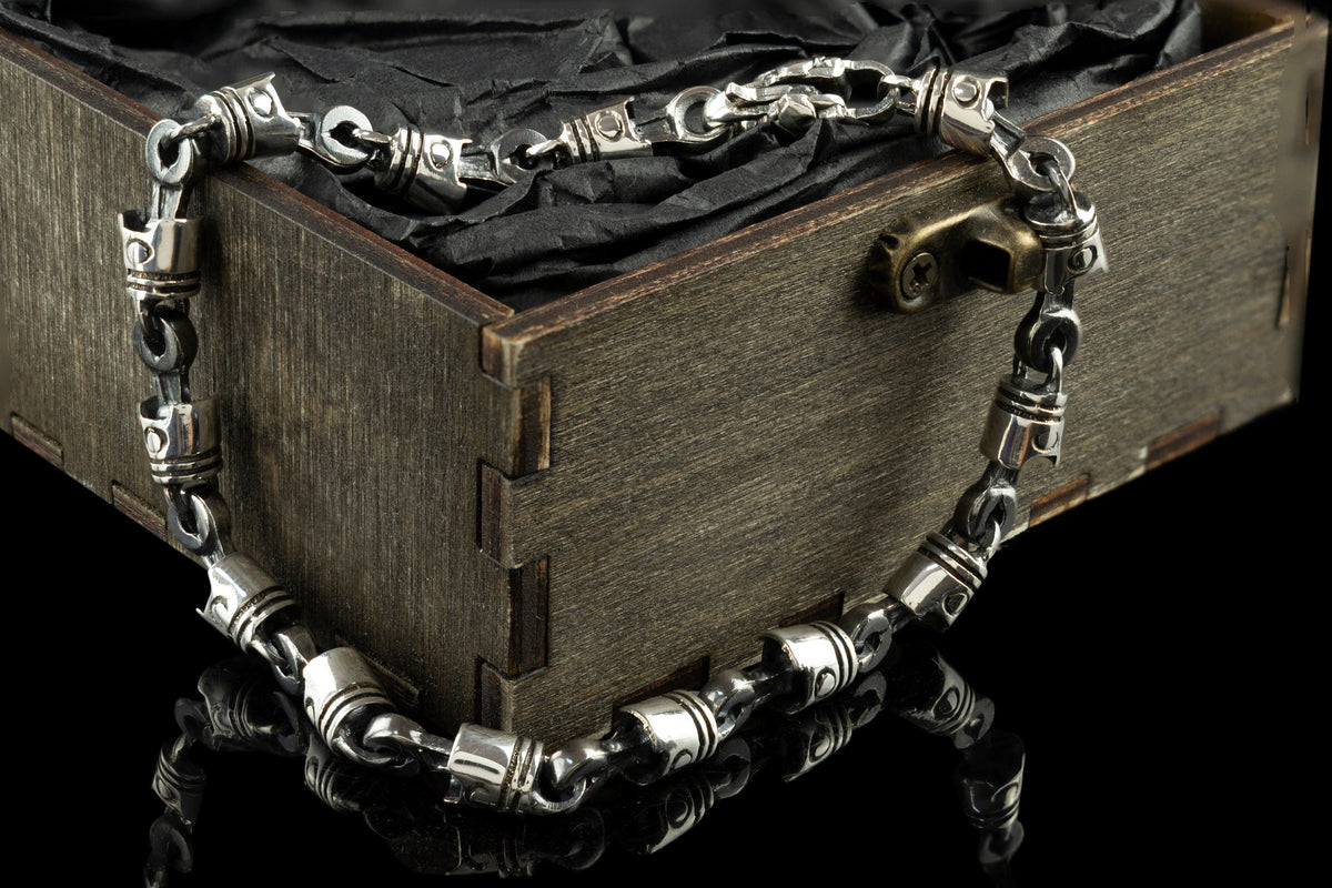 Piston and rod sterling silver biker bracelet draped over a wooden box