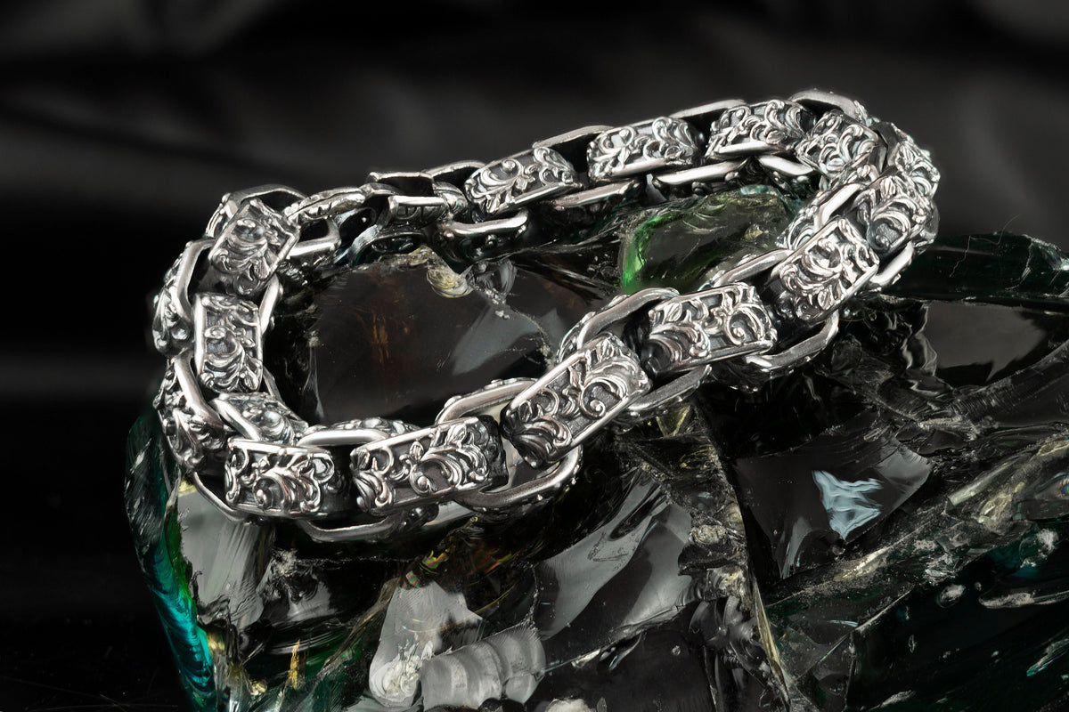 Rory ornate silver biker bracelet laid in a loop, polished edges and dark textured ornament