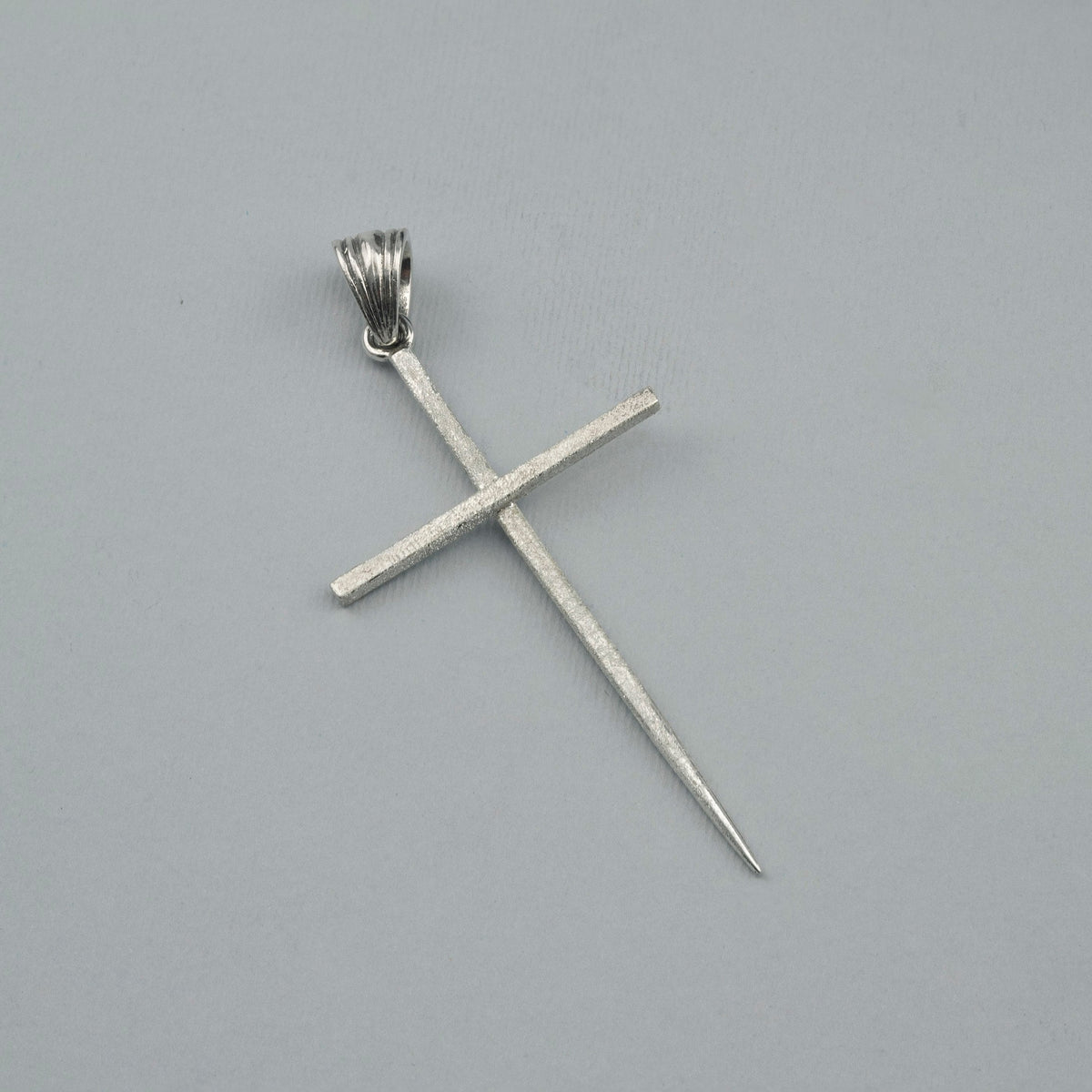 Long sterling silver spike cross pendant with ribbed bail on a light background
