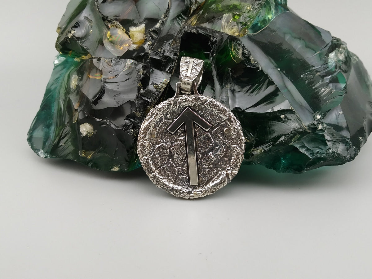 Round silver pendant with Tiwaz rune arrow on a textured oxidized background
