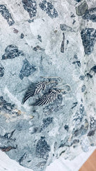 Close-up of silver angel wing drop earrings with oxidized feathers on stone