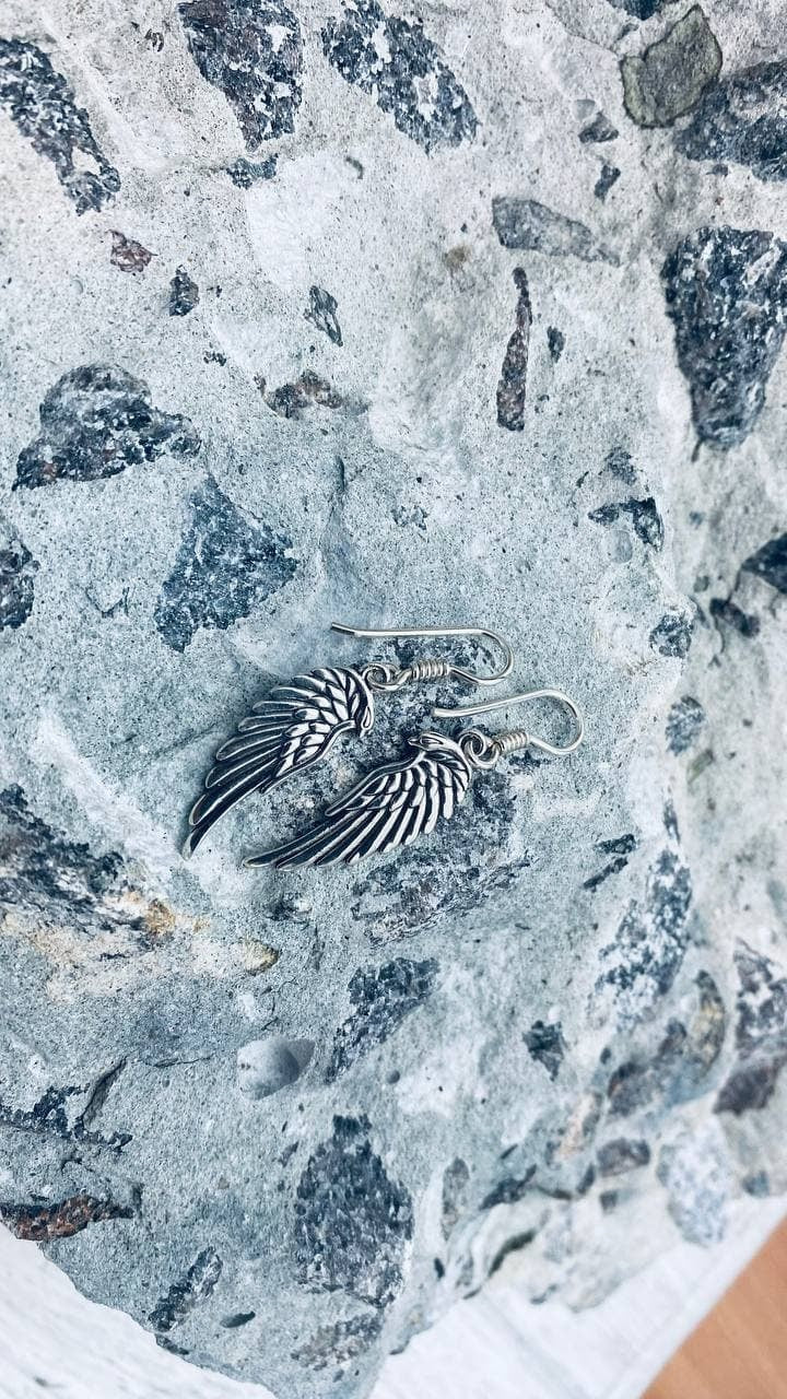 Close-up of silver angel wing drop earrings with oxidized feathers on stone