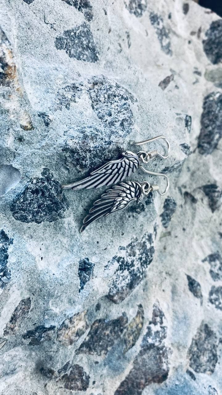Angel wing silver earrings laid side by side on a gray stone surface