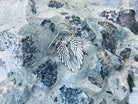 Angel wings sterling silver drop earrings on French ear wires, lying on gray stone