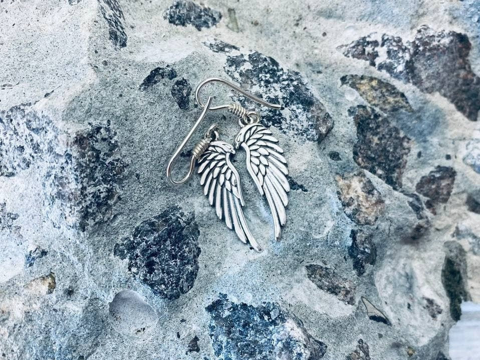 Angel wings sterling silver drop earrings on French ear wires, lying on gray stone
