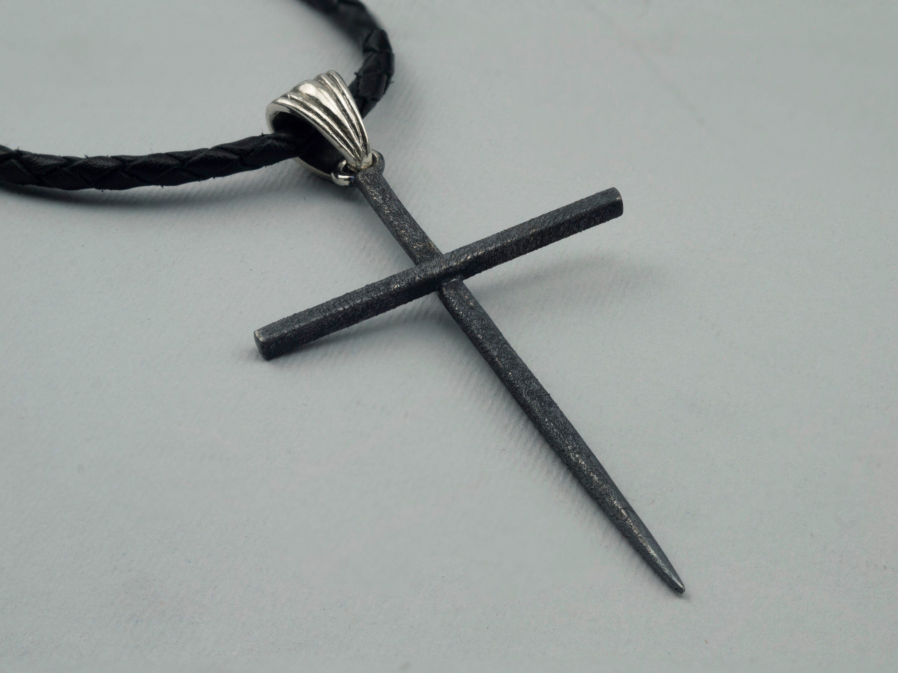 Close-up of the matte black spike cross pendant and polished ribbed bail on leather cord