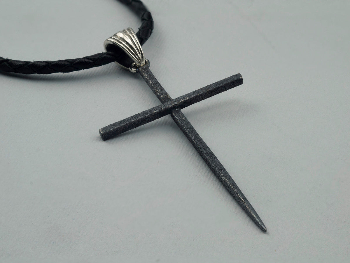 Close-up of the matte black spike cross pendant and polished ribbed bail on leather cord