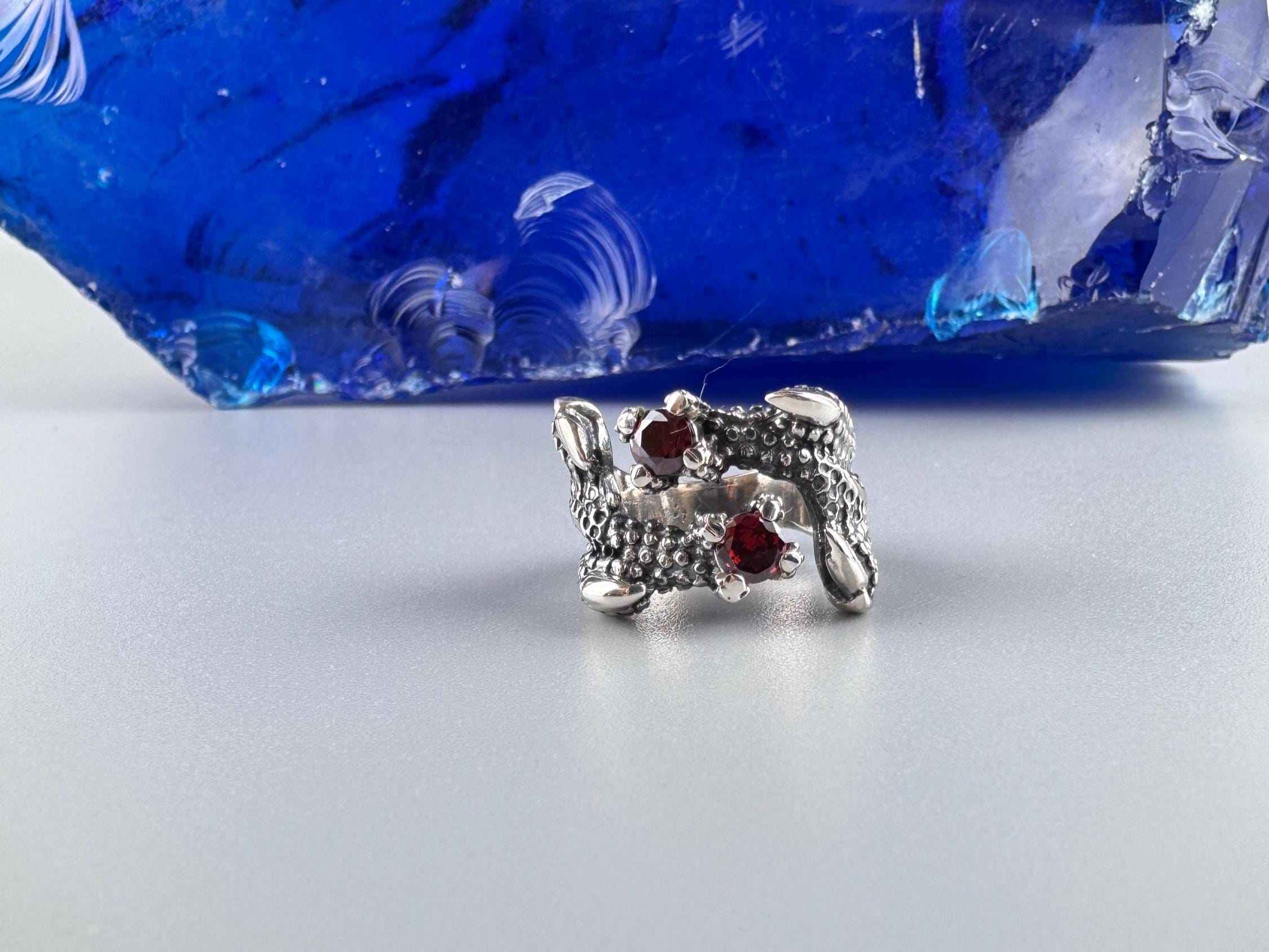 Dragon claw bypass ring in oxidized silver holding red garnets, angled view
