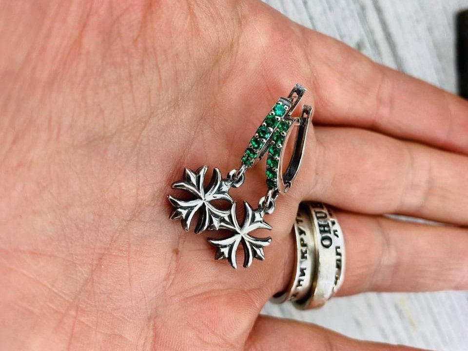 Crystal Maltese Cross earrings with green CZ hoops held in an open hand