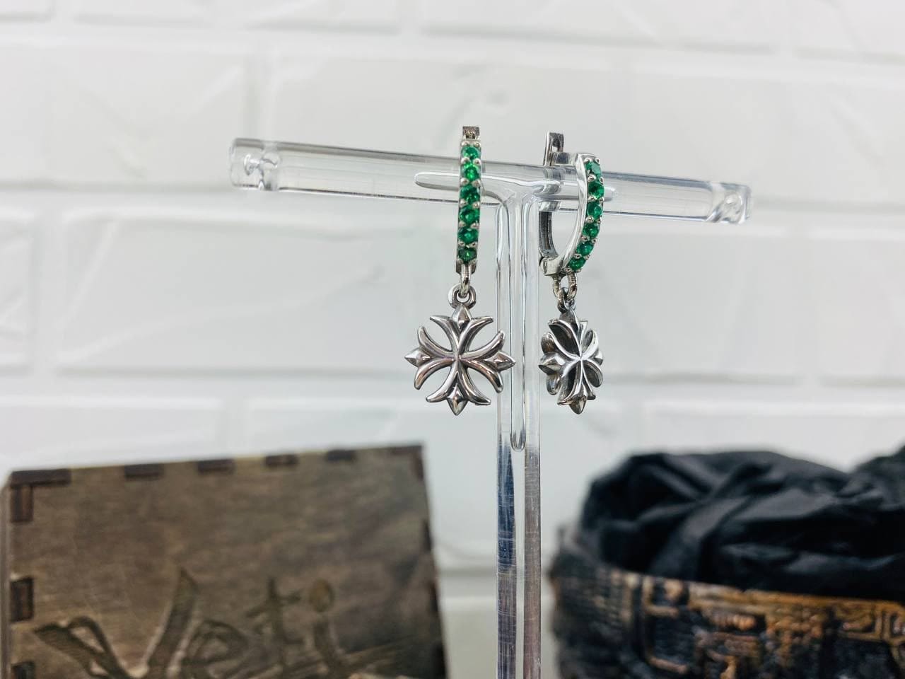 Crystal Maltese Cross earrings with green CZ leverbacks hanging on a clear display stand