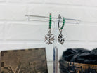 Crystal Maltese Cross earrings with green CZ leverbacks hanging on a clear display stand