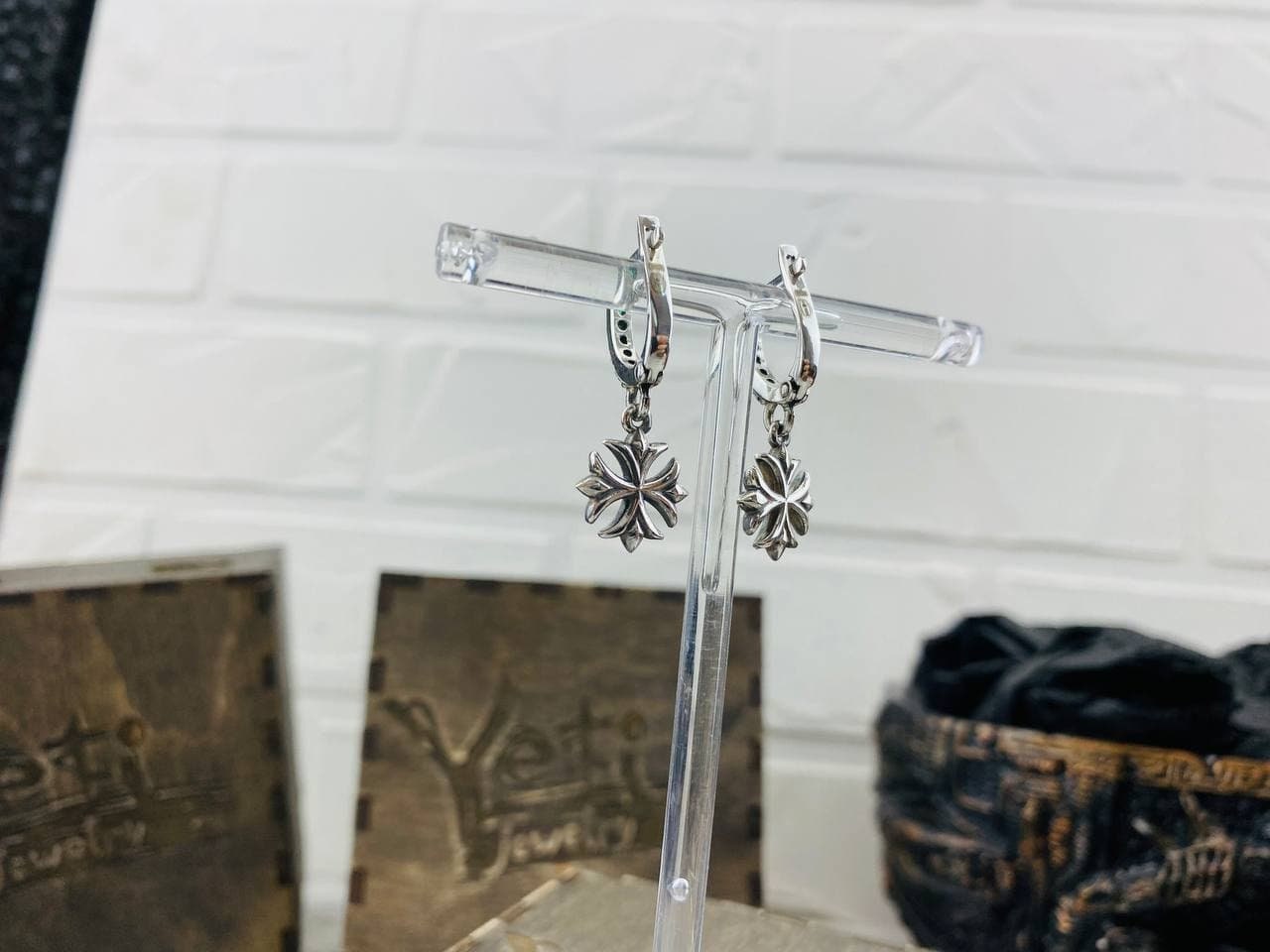 Maltese Cross drop earrings on a display stand beside wooden gift boxes