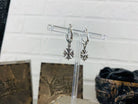 Maltese Cross drop earrings on a display stand beside wooden gift boxes