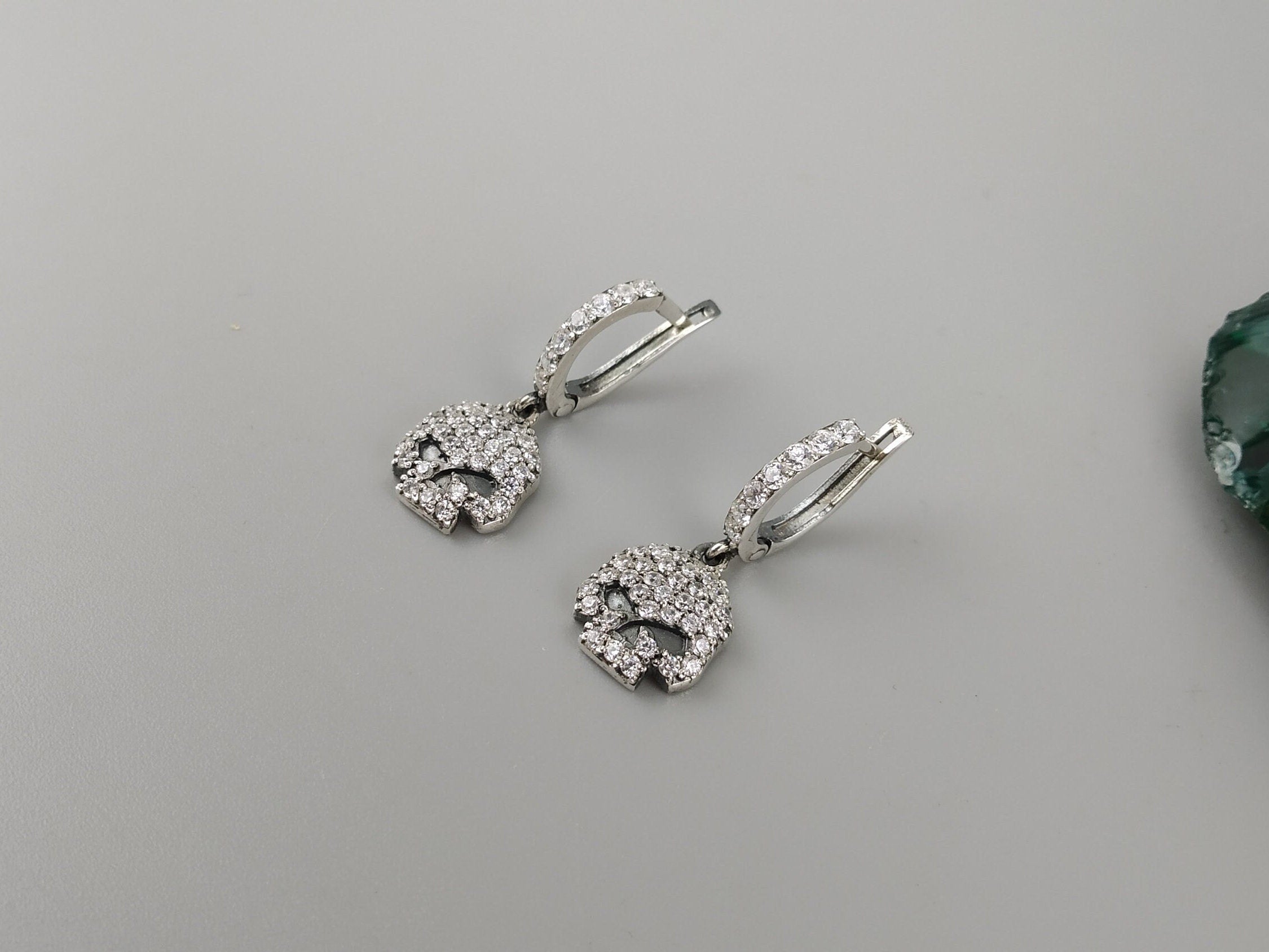 Pair of pave CZ skull drop earrings lying flat on a gray background