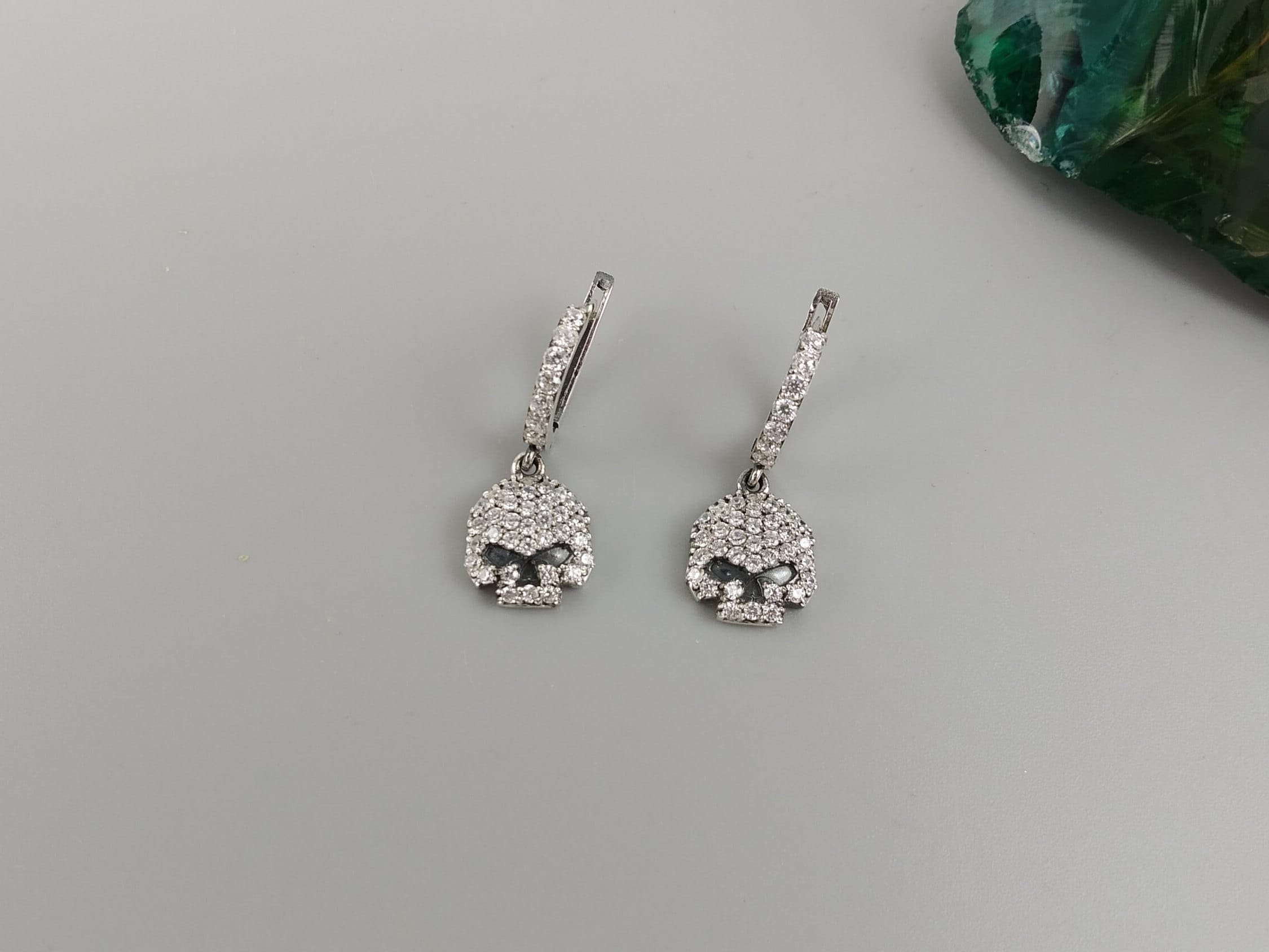 Crystal Skull earrings on a gray background with a green stone in the corner