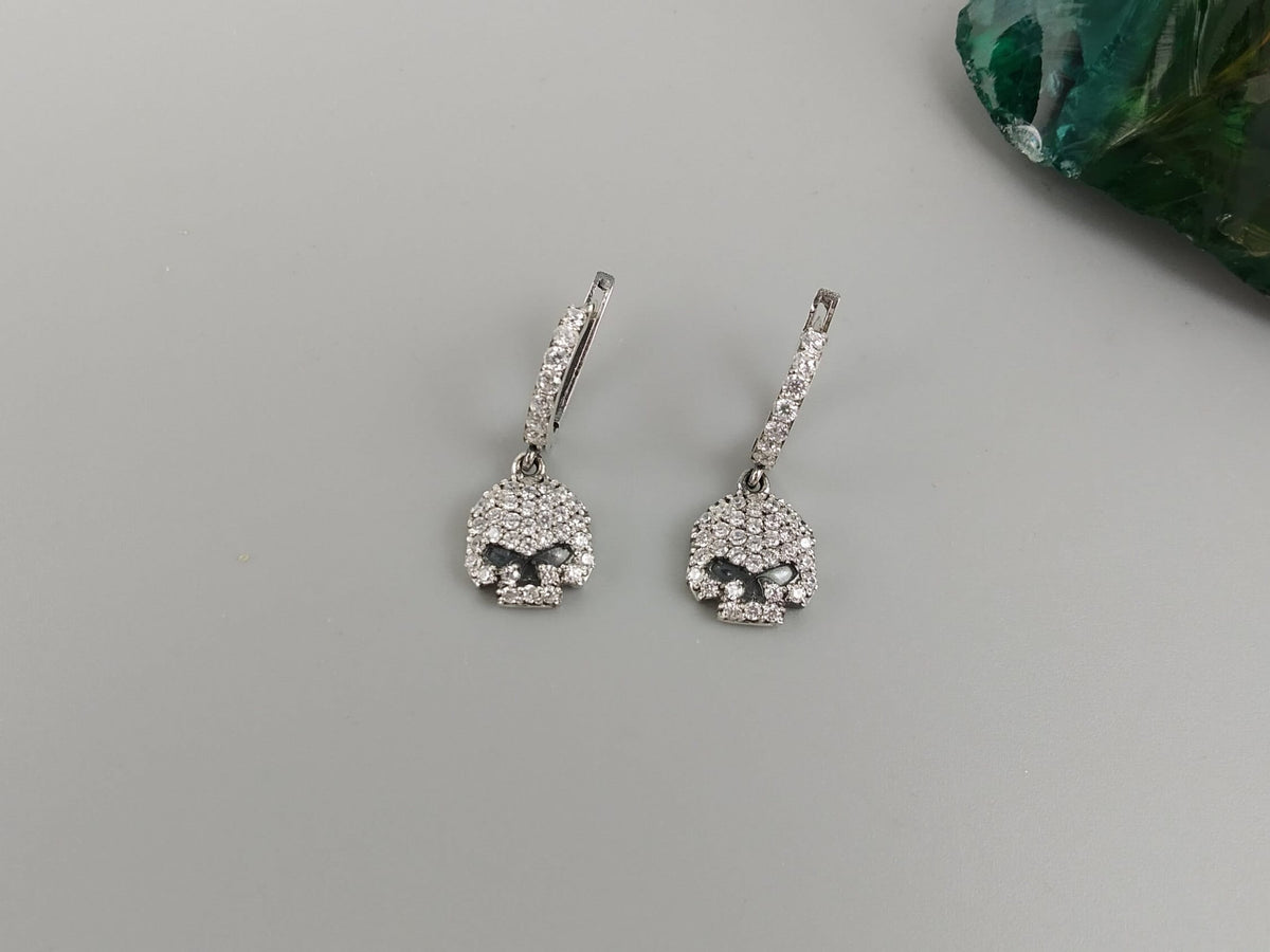 Crystal Skull earrings on a gray background with a green stone in the corner