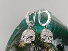 Crystal Skull CZ drop earrings hanging over a green glass stone