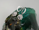 Crystal Skull earrings hanging on a green glass stone, side angle