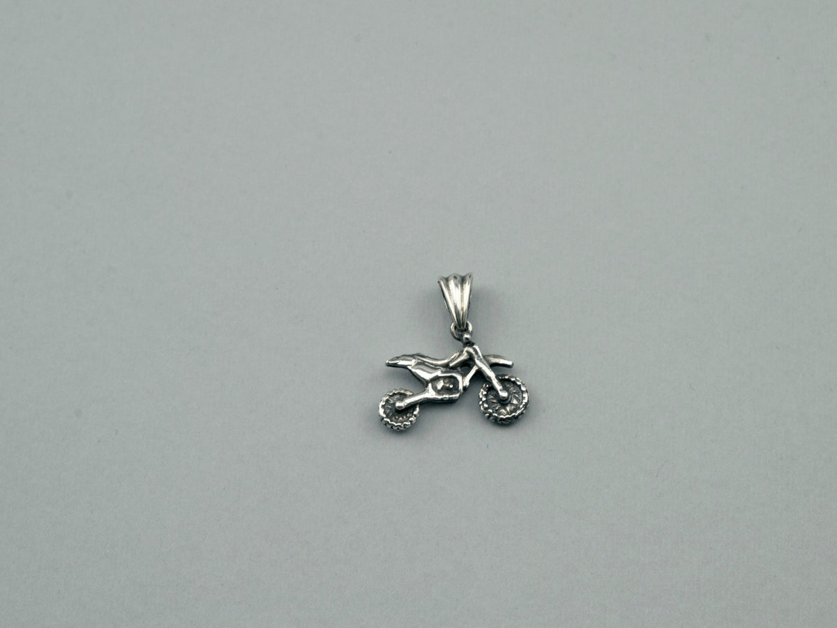 Small sterling silver motocross pendant lying flat on a light background