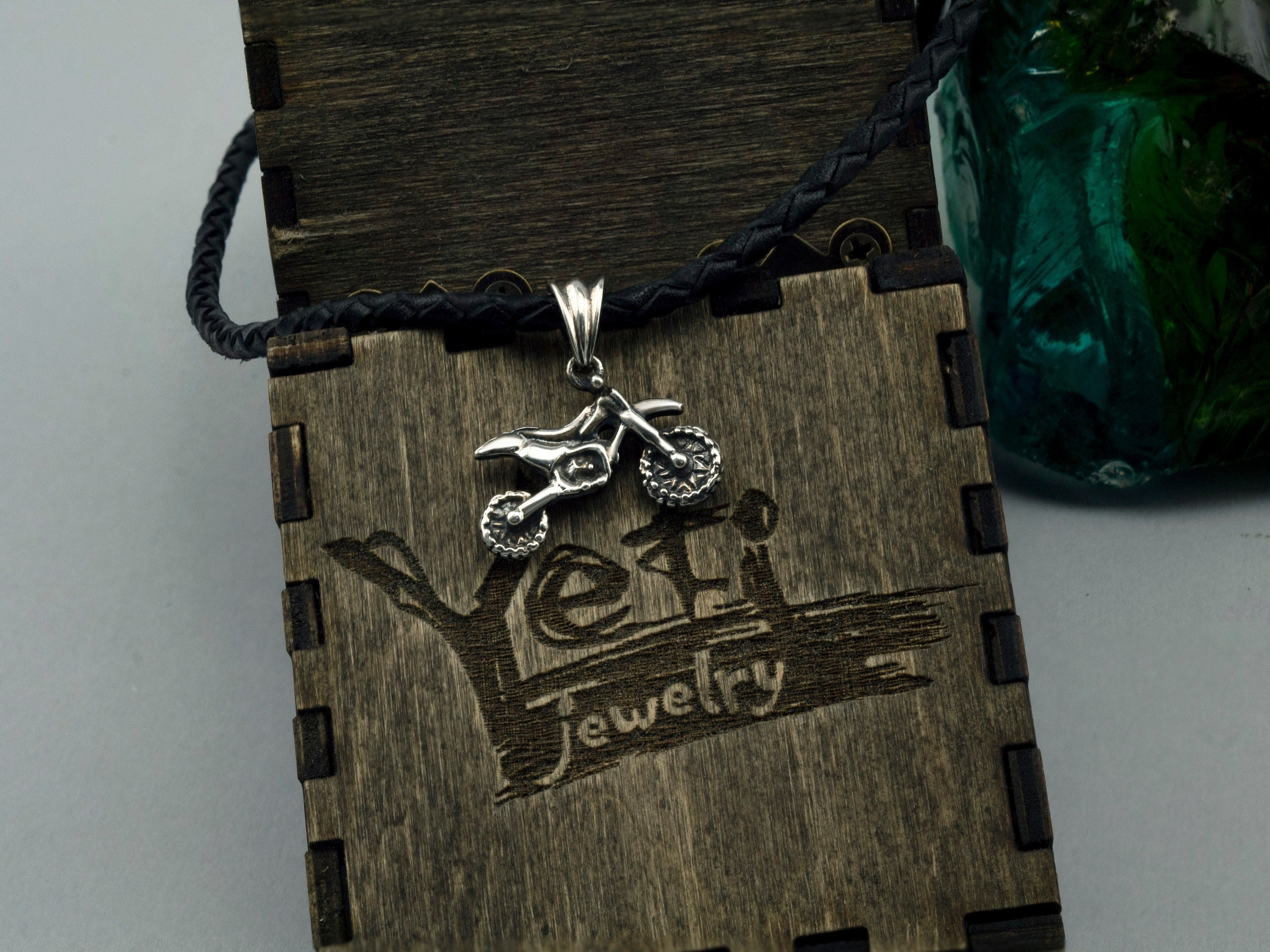 Enduro motorcycle sterling silver pendant on a black cord against a wooden Yeti box
