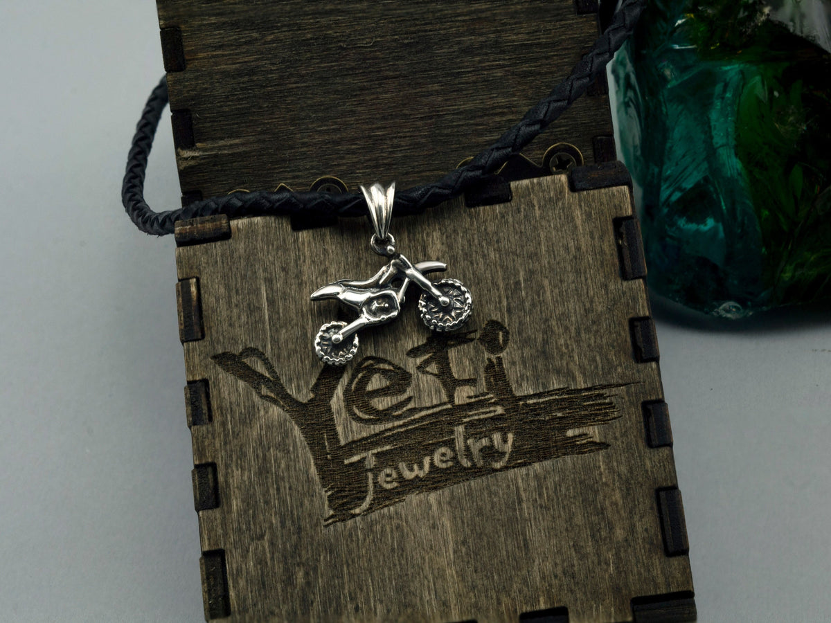 Enduro motorcycle sterling silver pendant on a black cord against a wooden Yeti box
