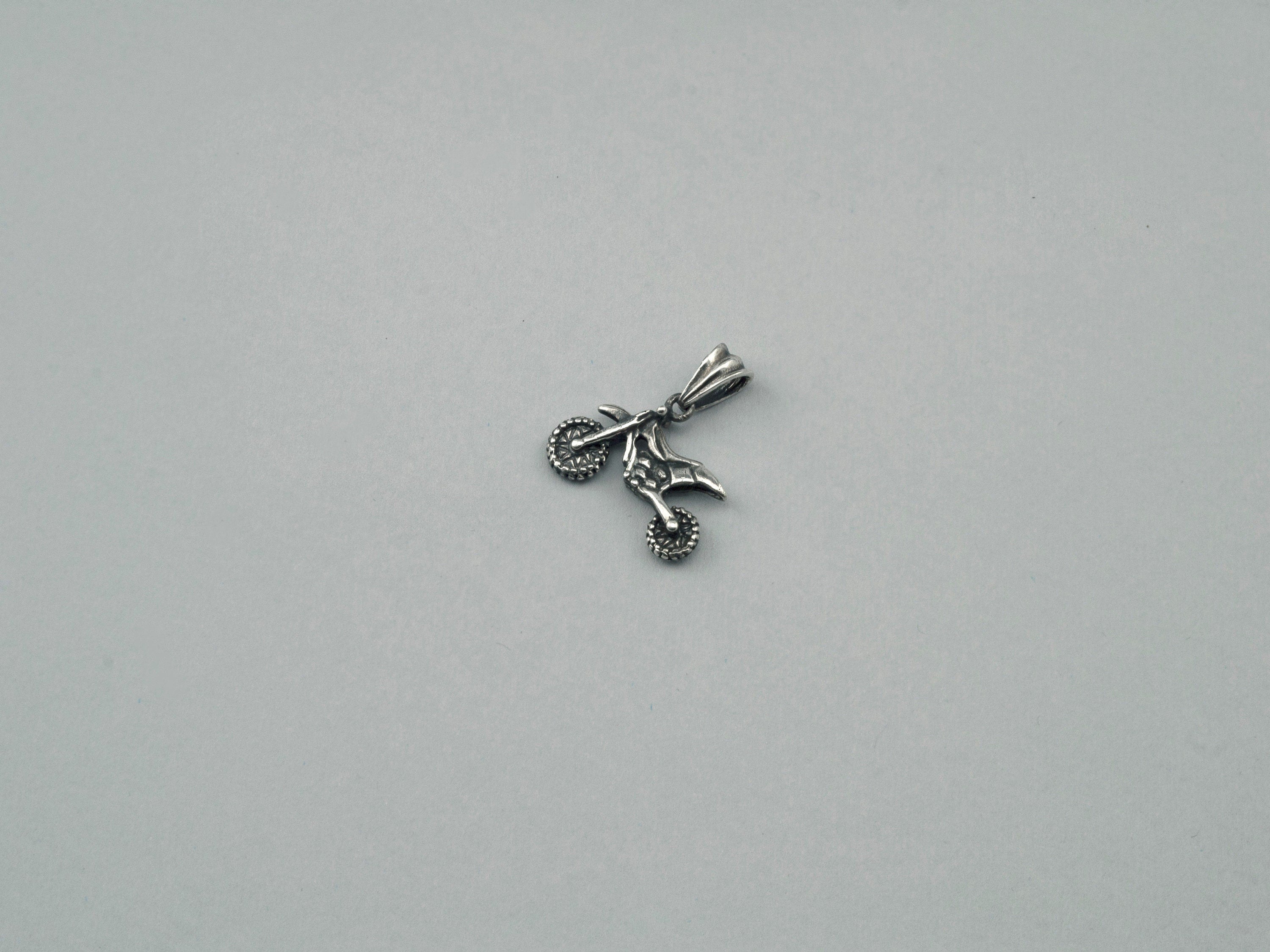 Side view of the silver enduro motorcycle pendant showing wheels and frame
