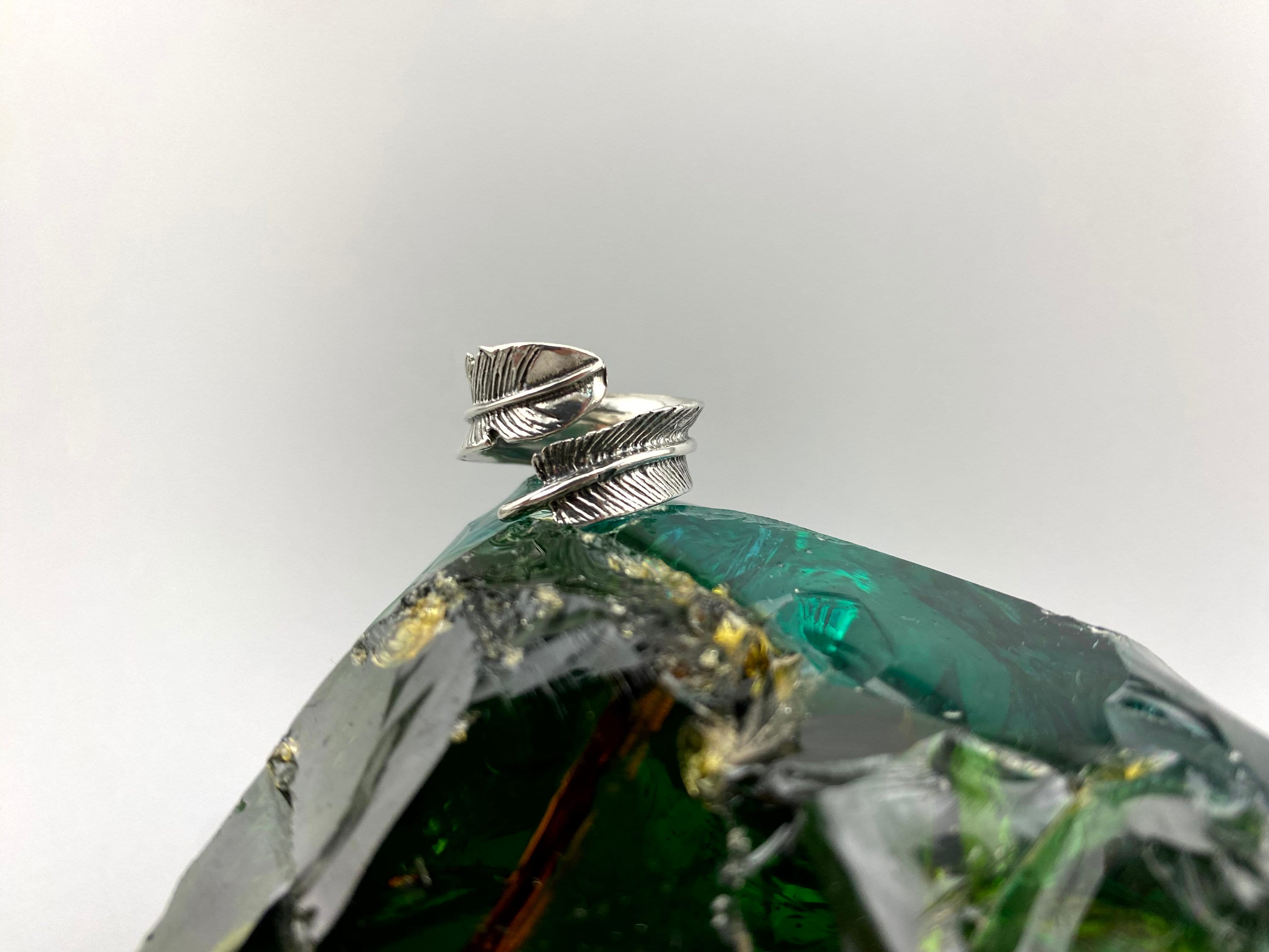 Silver feather ring standing on its band, side view of the two feathers