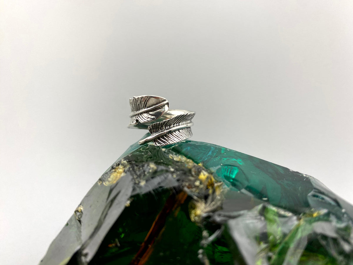 Silver feather ring standing on its band, side view of the two feathers
