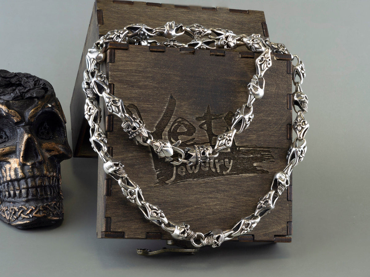 Fleur de lis skull sterling silver chain on a wooden box beside a skull figure