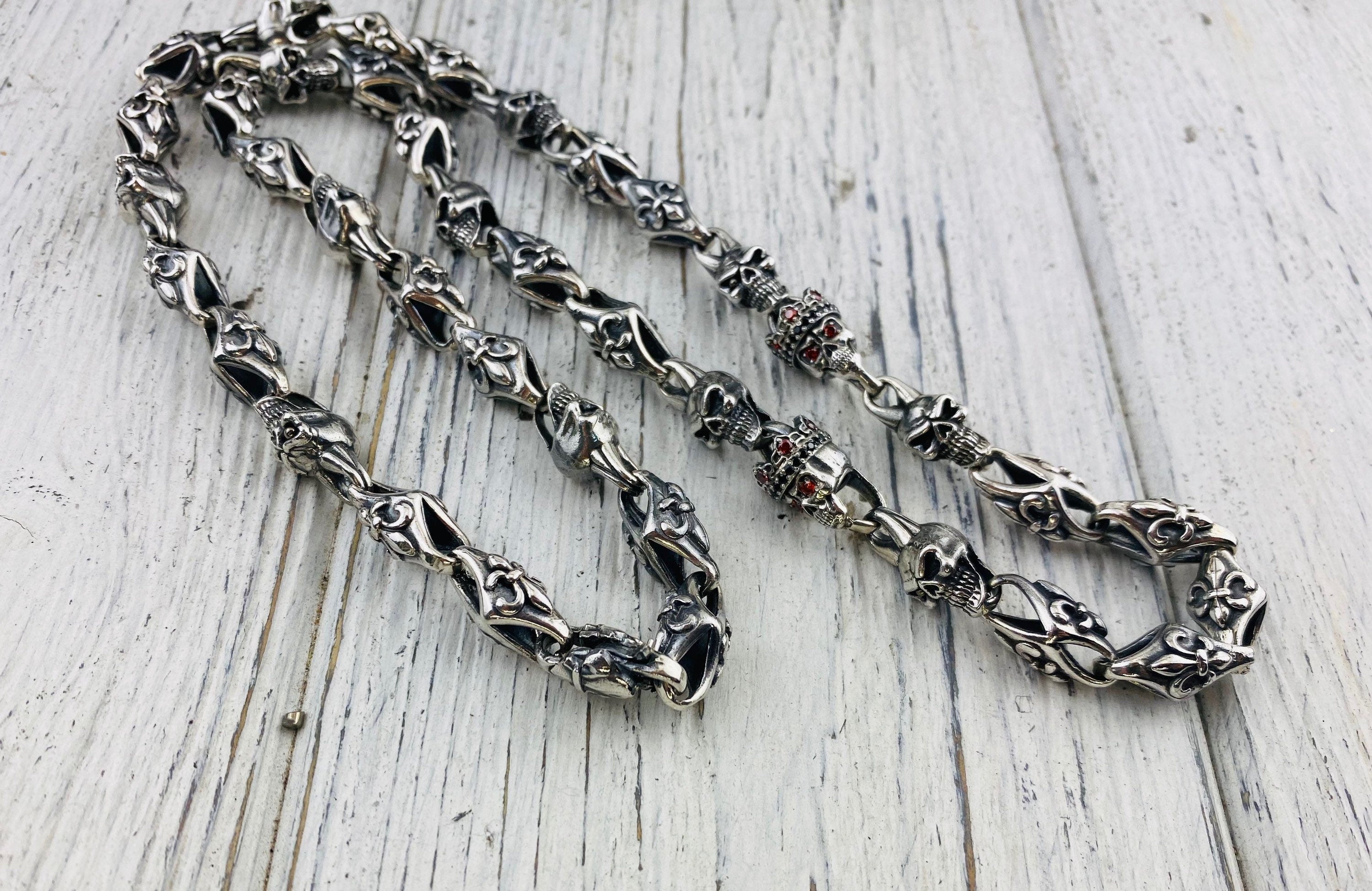 Close-up of fleur-de-lis and crowned skull links on white wood