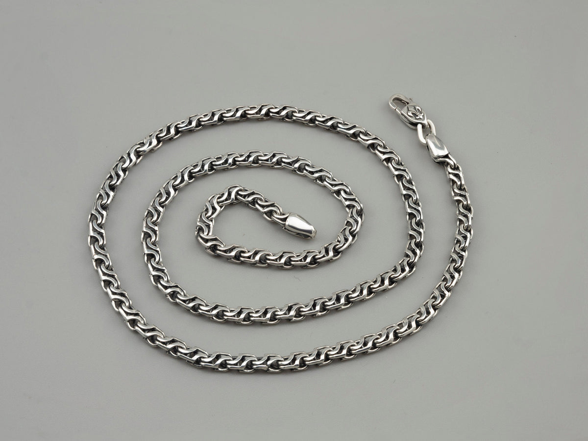Forge sterling silver chain coiled in a spiral on a gray background