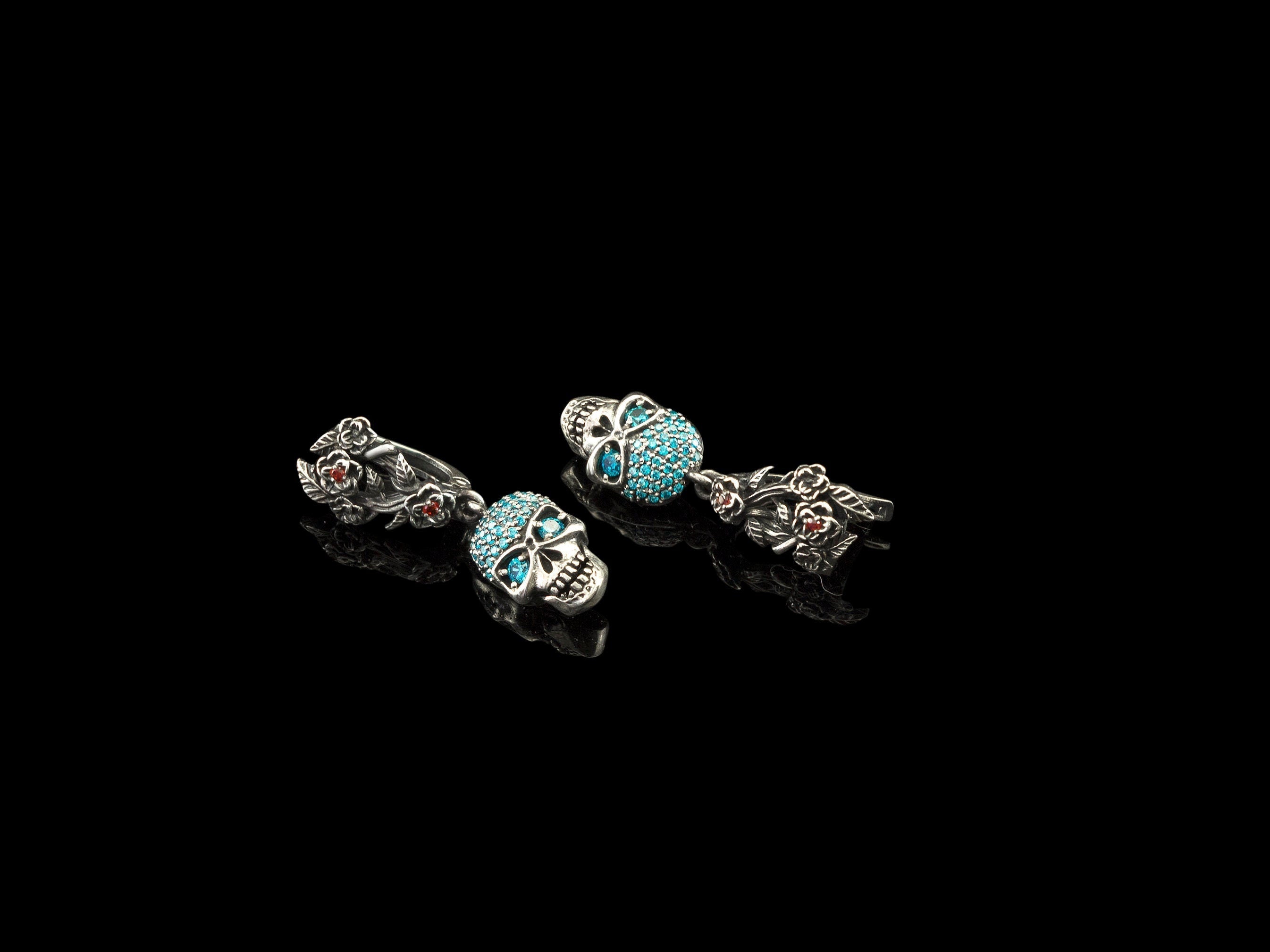 Frida Light skull earrings with blue CZ and floral leverbacks laid flat on black