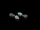 Frida Light skull earrings with blue CZ and floral leverbacks laid flat on black