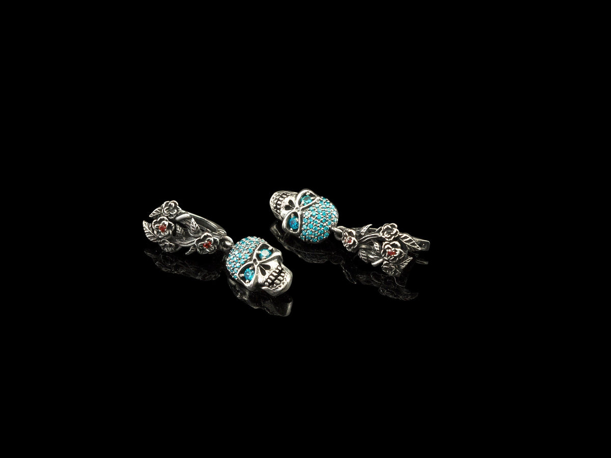Frida Light skull earrings with blue CZ and floral leverbacks laid flat on black