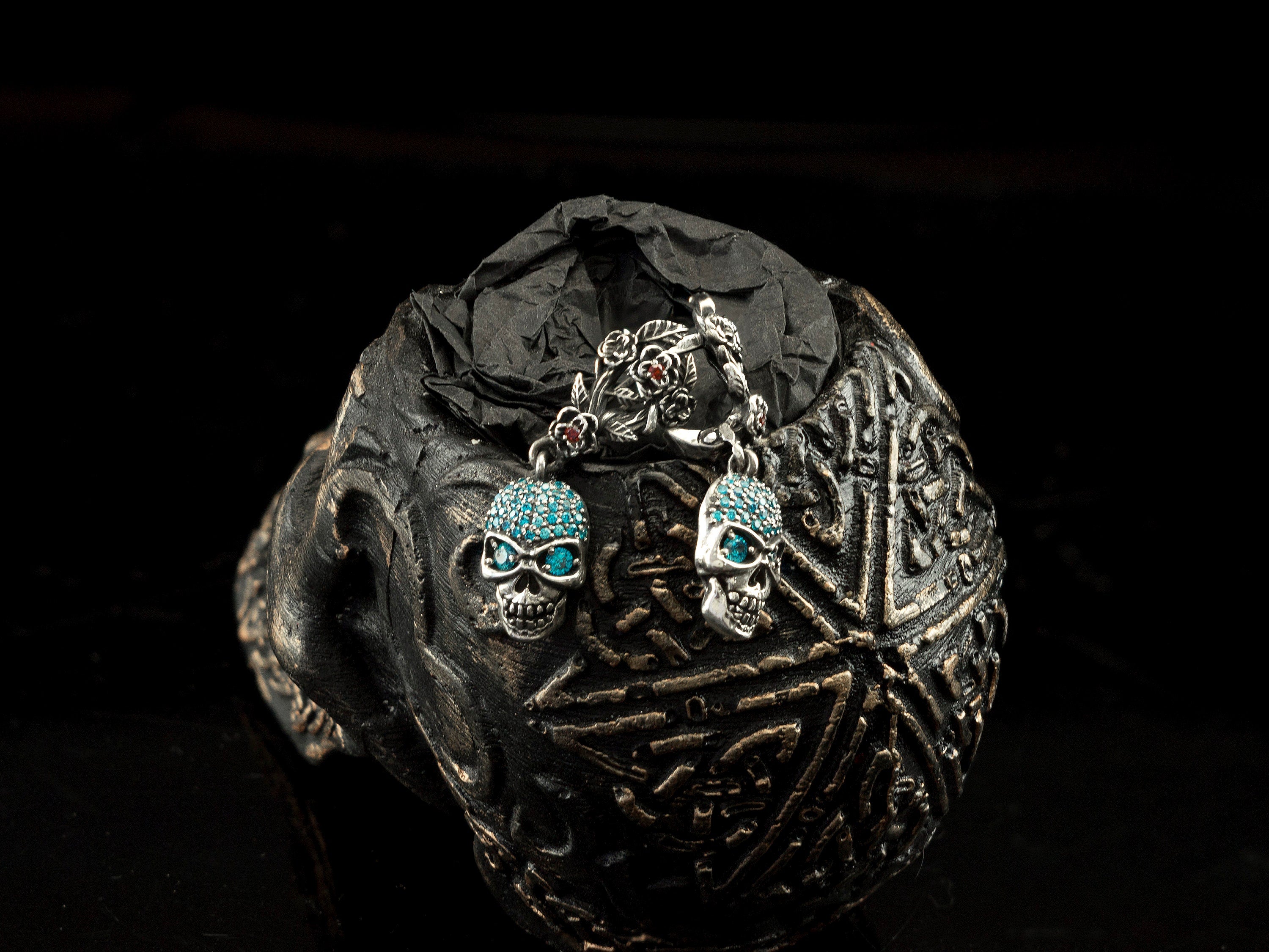 Frida Light blue CZ skull earrings resting on a carved skull, top view